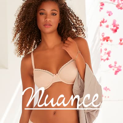 Nuance – Frau mit lockigem Haar in hellem BH und Slip, hält grauen Stoff, Hintergrund mit rosa Blütenmuster