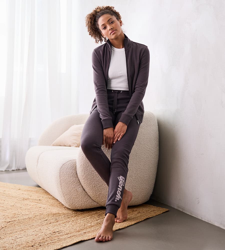 Frau in Freizeitanzug sitzt entspannt auf einem cremefarbenen Sessel, ihre Füße berühren den hellen Teppich.