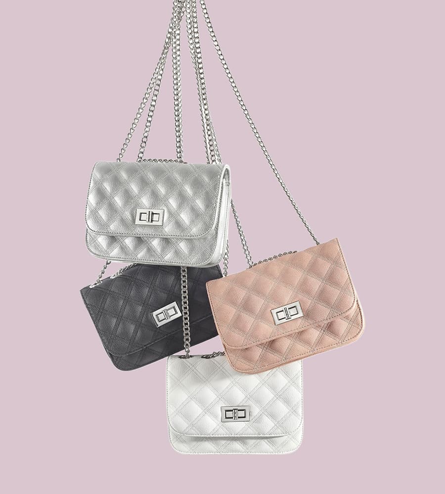 Vier gesteppte Handtaschen in Silber, Schwarz, Rosa und Weiß hängen an silbernen Ketten vor einem hellvioletten Hintergrund