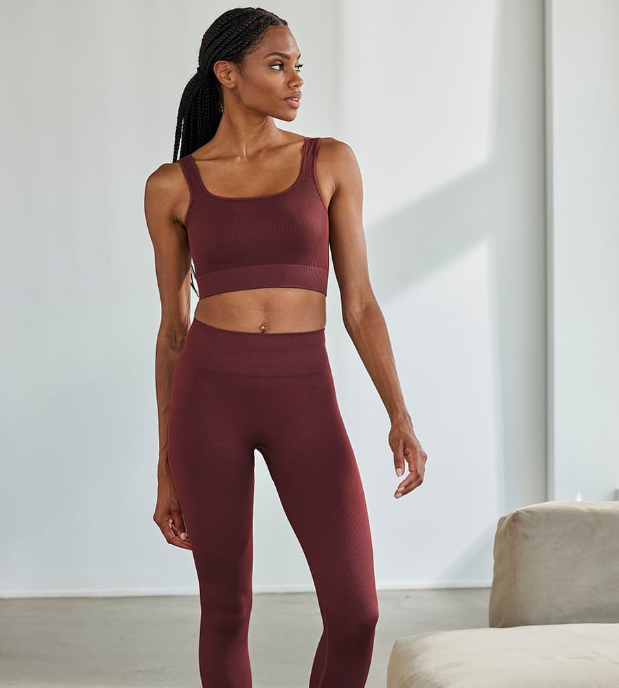 Frau in bordeauxfarbenem Sport-BH und Leggings steht in einem hellen Raum