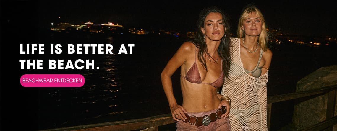 LIFE IS BETTER AT THE BEACH. BEACHWEAR ENTDECKEN – Zwei Frauen in Strandkleidung posieren nachts am Wasser.