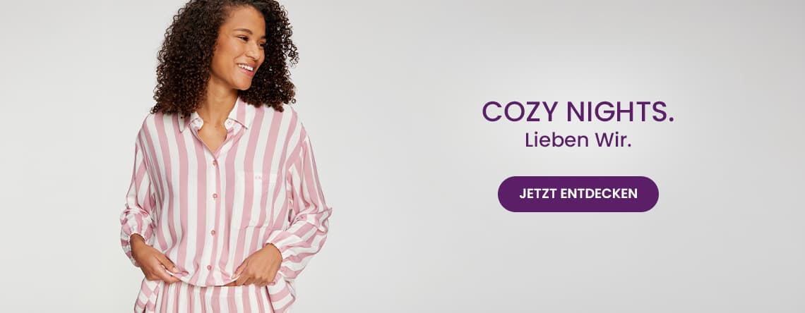 COZY NIGHTS. Lieben Wir. Jetzt entdecken – Frau in gestreiften Pyjama schaut in die Kamera