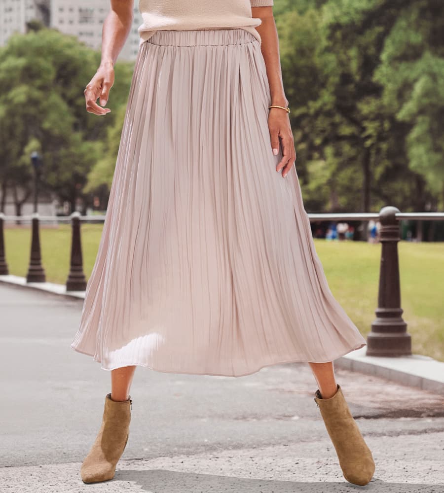 Frau trägt einen langen, fließenden Rock und Stiefeletten, spaziert in einem Park.