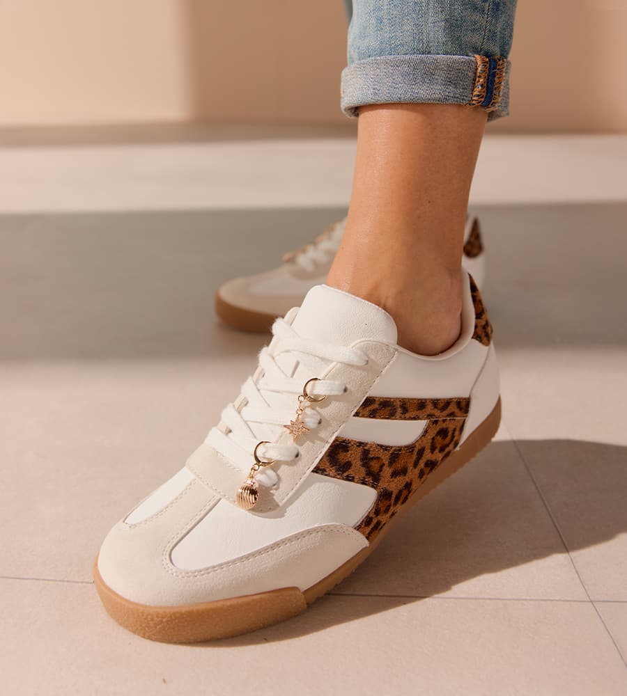 Weiße Sneaker mit Leopardenmuster und kleinen Anhängern an den Schnürsenkeln, getragen zu hochgekrempelter Jeans