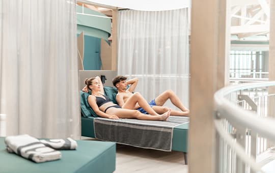 Paar in Badekleidung liegt auf einer Liege in einer Kabine mit Vorhängen im Wellnessbereich