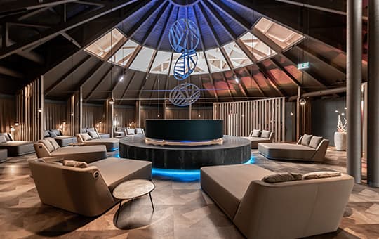 Runder Ruheraum mit Liegesofas im Kreis, zentraler runder Bereich und moderne Lichtinstallation unter Kuppeldach