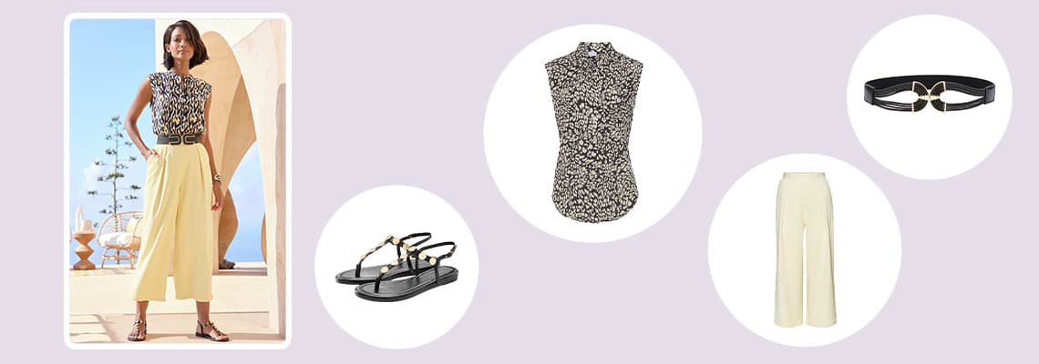 Frau in gemustertem ärmellosem Top, weiter hellgelber Hose, Sandalen und Gürtel steht draußen vor moderner Architektur