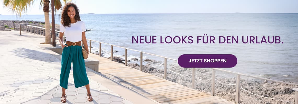 Neue Looks für den Urlaub – Frau in weißem Shirt und türkisfarbener Hose steht an der Promenade mit Meer im Hintergrund