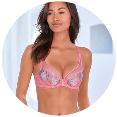 Frau in rosa BH mit buntem Muster steht seitlich und blickt lächelnd nach rechts